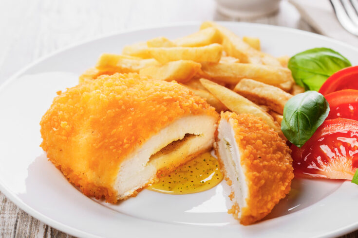Air fryer frozen chicken kiev on a white plate with fries and salad.