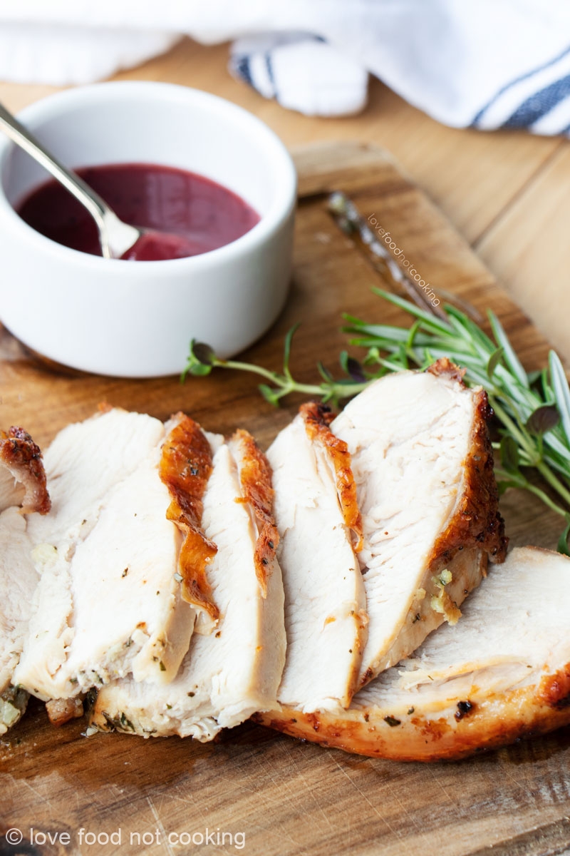 Sliced air fryer turkey breast on a wooden board with cranberry sauce.