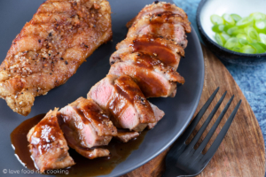 Two air fryer duck breasts on a greay plate, one is sliced with hoisin sauce. Looks delicious.