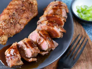 Two air fryer duck breasts on a greay plate, one is sliced with hoisin sauce. Looks delicious.