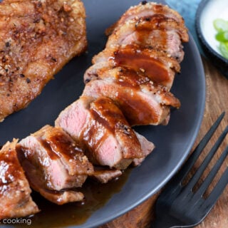 Two air fryer duck breasts on a greay plate, one is sliced with hoisin sauce. Looks delicious.