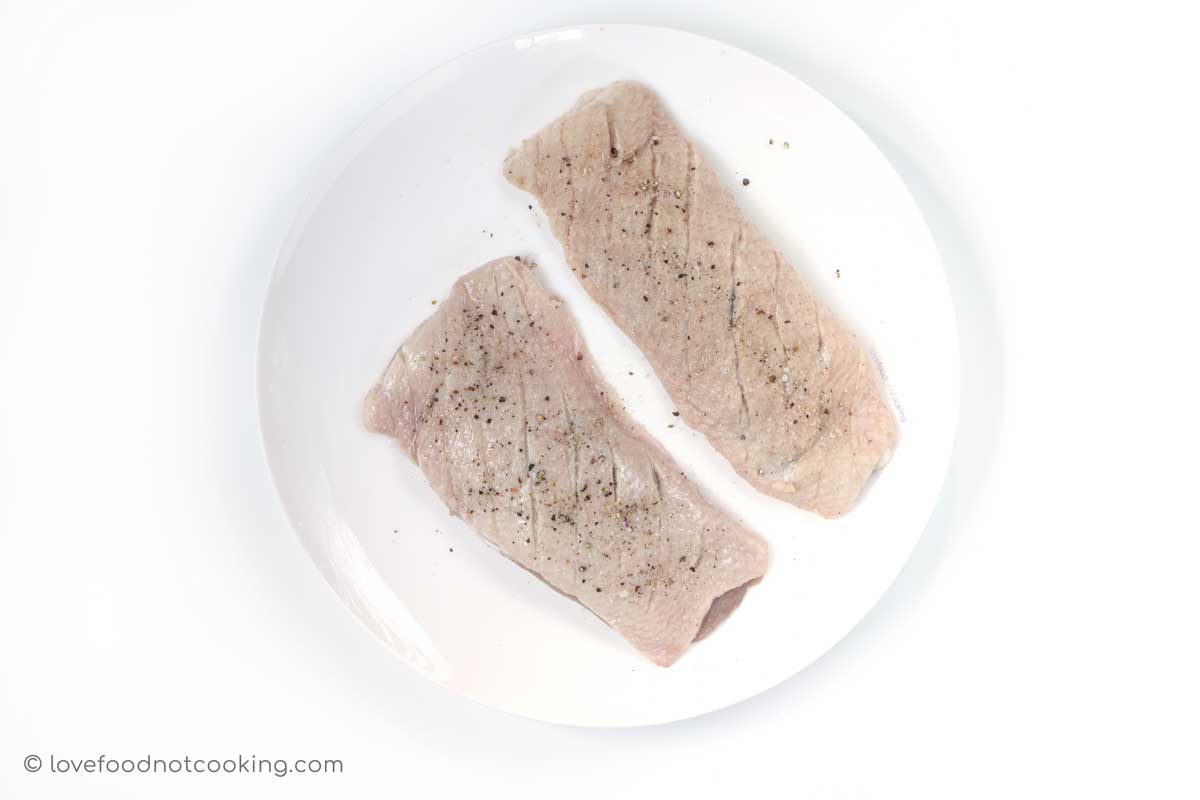 Seasoned duck breasts on a white plate. 