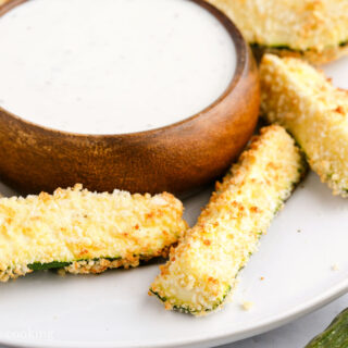 Air fryer zucchini fries on a white plate with ranch dressing.