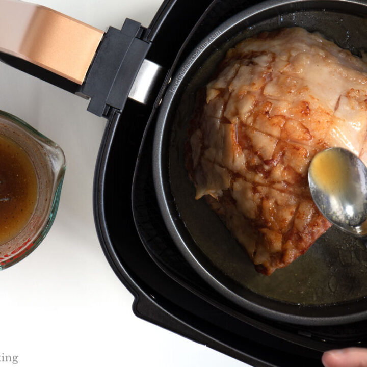 A hand basting the ham in the air fryer.