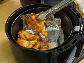 Chicken wings being put in an air fryer with foil.