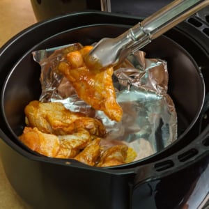 Chicken wings being put in an air fryer with foil.