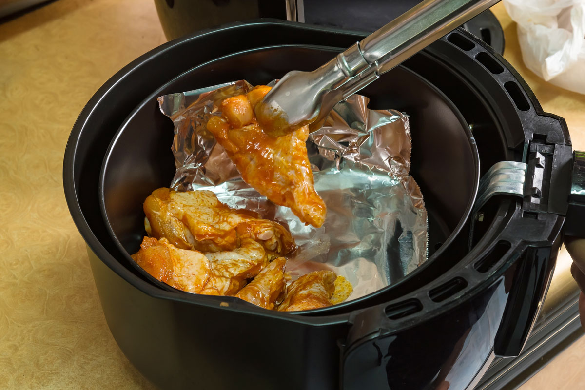 Chicken wings being put in an air fryer with foil. 