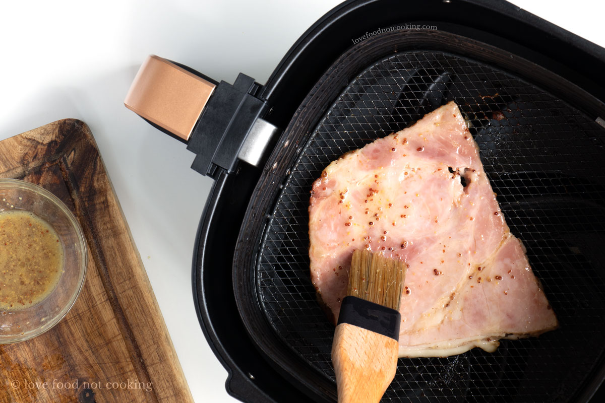 Ham steak in air fryer being brushed with glaze.