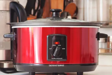 A bright red slow cooker on a kitchen bench.