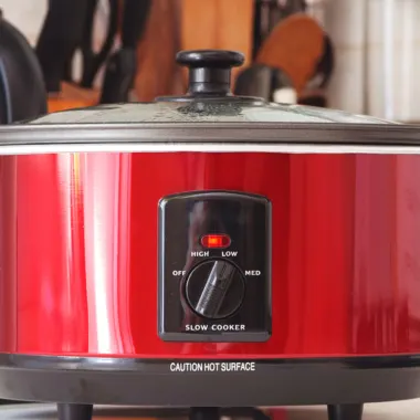 A bright red slow cooker on a kitchen bench.