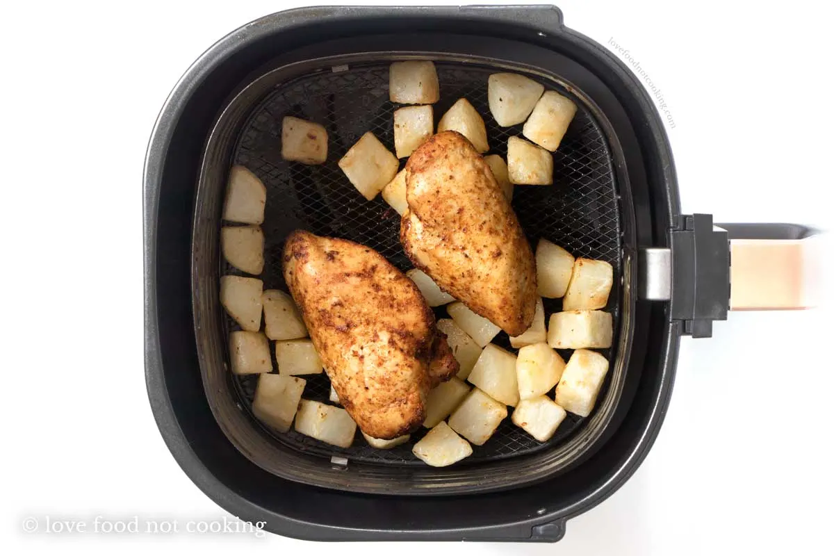 Cooked chicken and potatoes in the air fryer basket. 