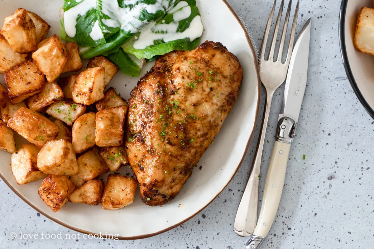 Air fryer chicken breast and potatoes on a white plate.