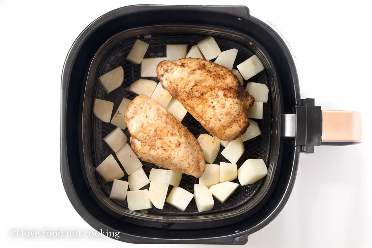 Chicken and potatoes in air fryer basket.