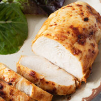 Air fried frozen chicken breast sliced on a plate with salad.