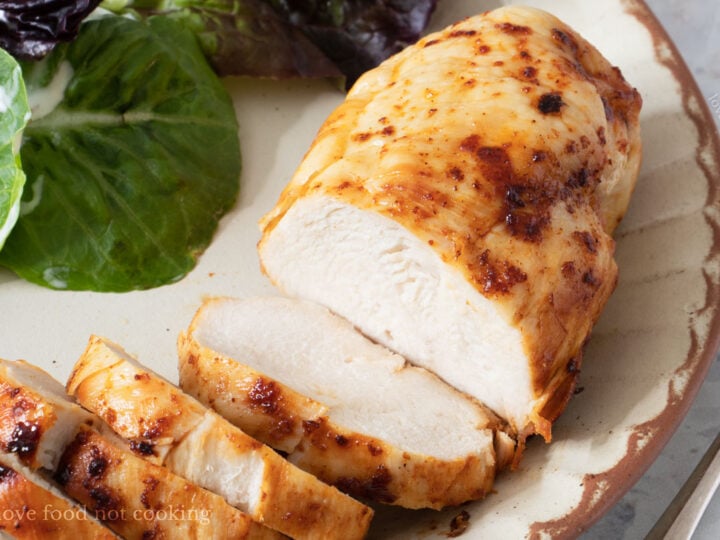 Air fried frozen chicken breast sliced on a plate with salad.