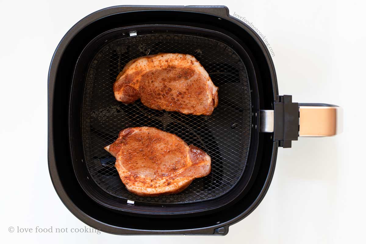 Two uncooked pork chops in air fryer basket.