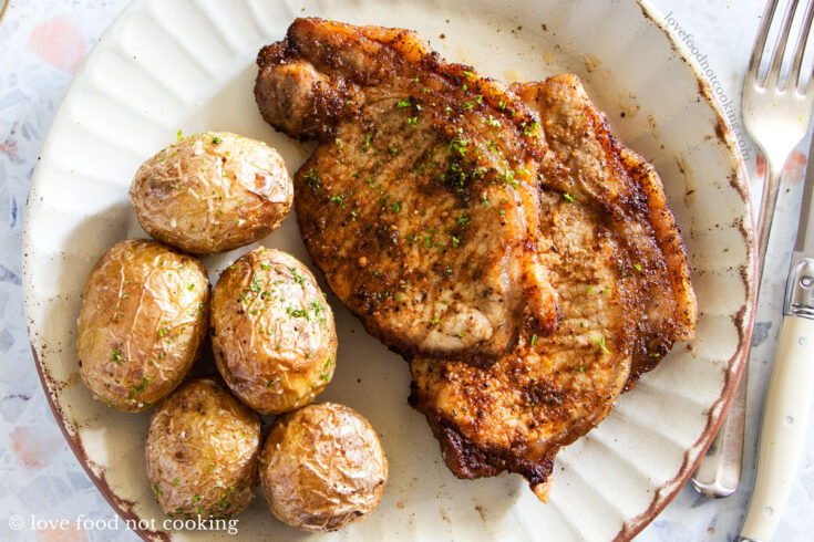 Air fryer pork chops and potatoes on a white plate.