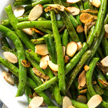 Air fryer green beans and toasted almond slices in a white bowl.