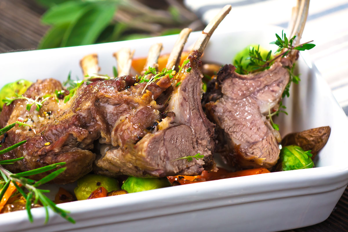 Lamb rack with roasted vegetables in a white dish. 