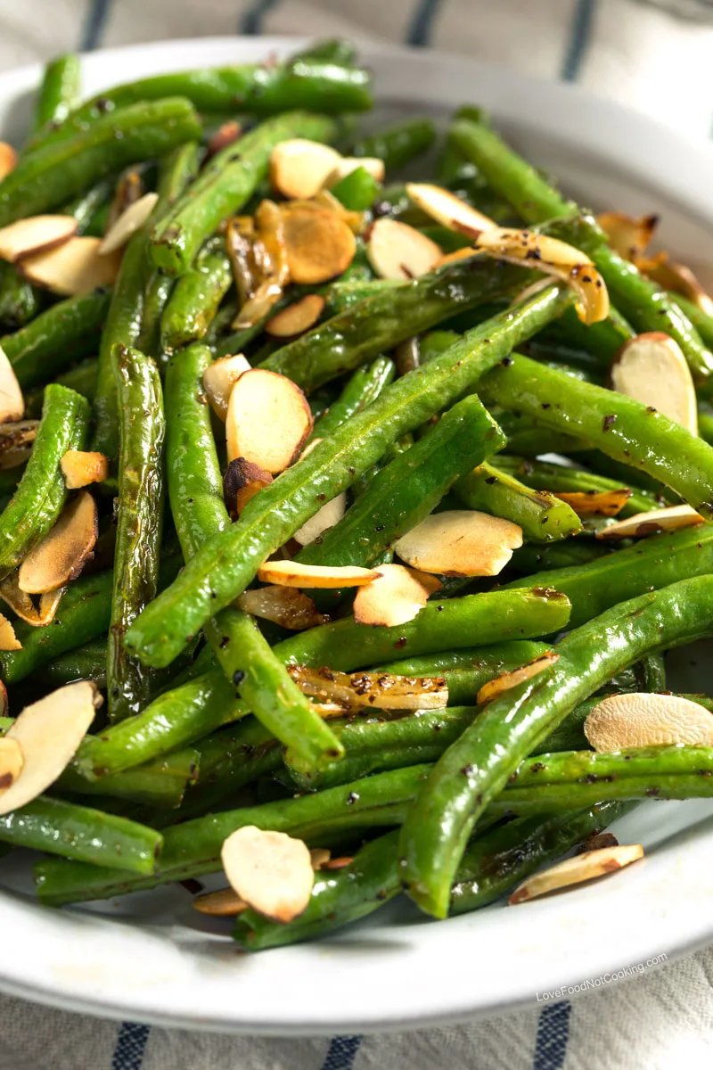 Air fried green beans in a white bowl served with toasted almond flakes.