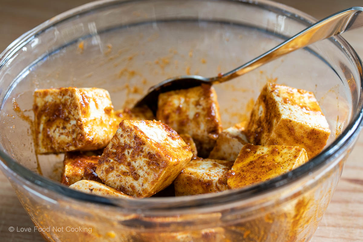 Tofu cubes coated in oil and seasoning in a glass bowl. 