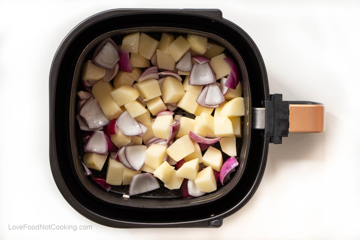 Raw potatoes and onions in air fryer basket. 