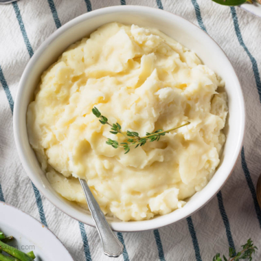 A white bowl of mashed potatoes on a table.