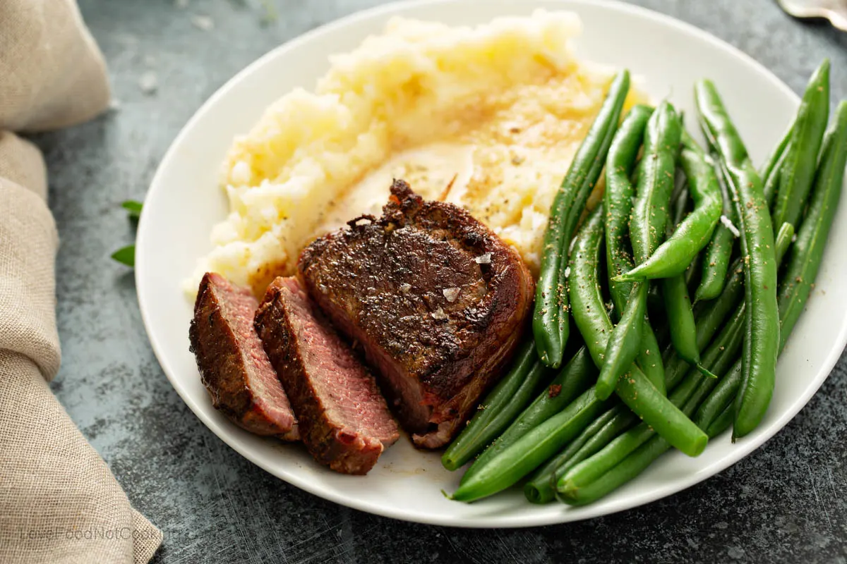 Steak with mashed potatoes and green beans on a white plate. 