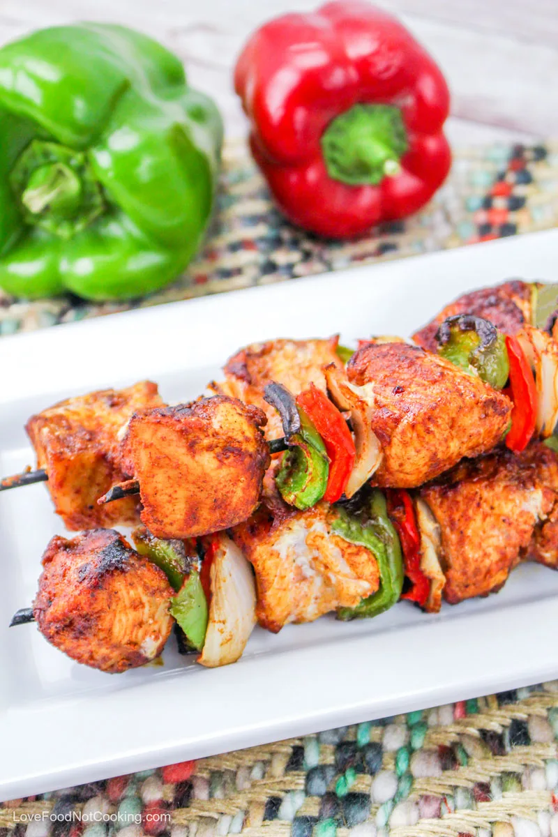 Air fried chicken kabobs on a white plate with red and green bell peppers. 