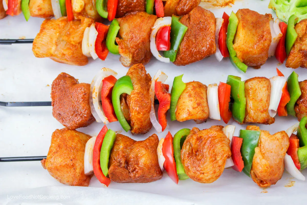Uncooked chicken kebabs with bell pepper and onion slices. 