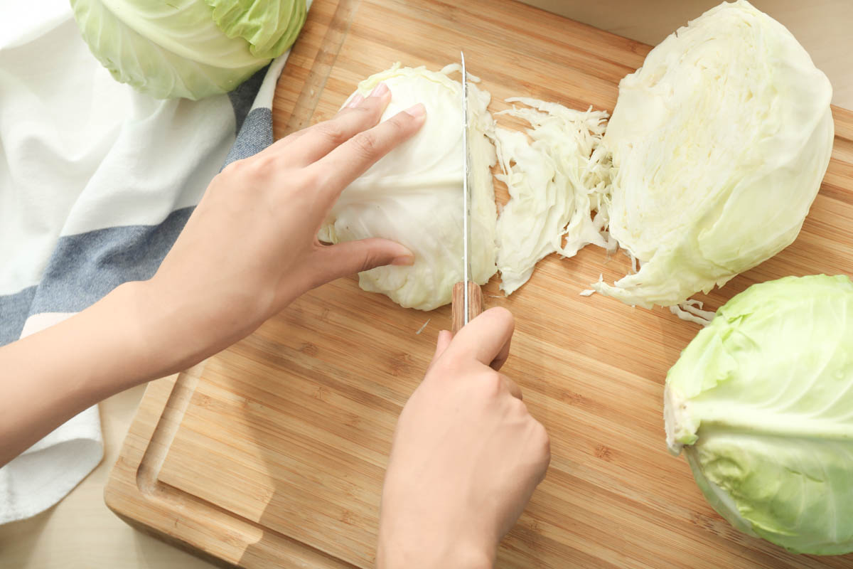 Hands slicing cabbage on a wooden board. 