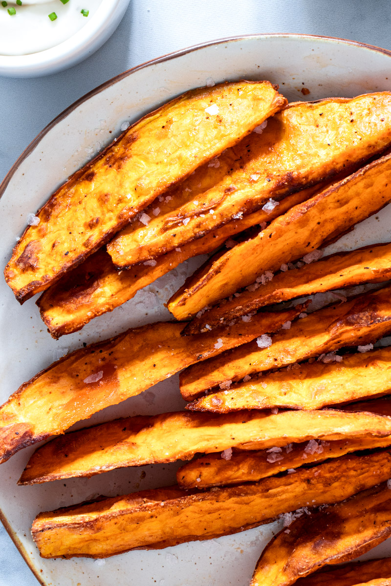 Air fried sweet potato wedges on a white plate with dipping sauce. 