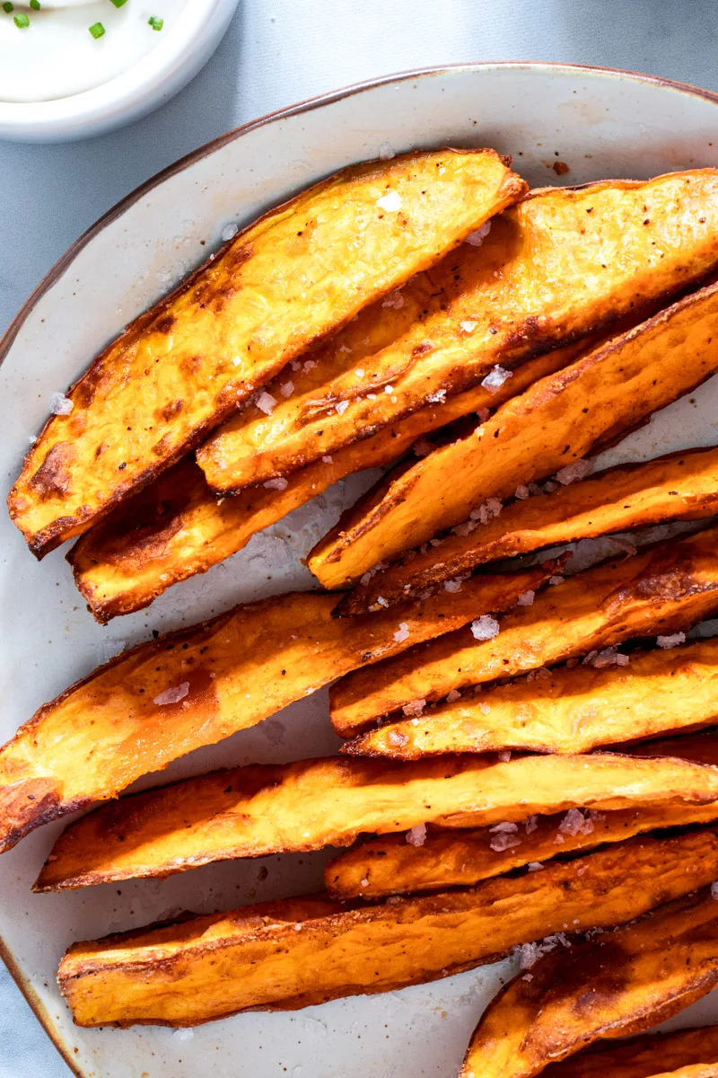 Air fried sweet potato wedges on a white plate with dipping sauce. 