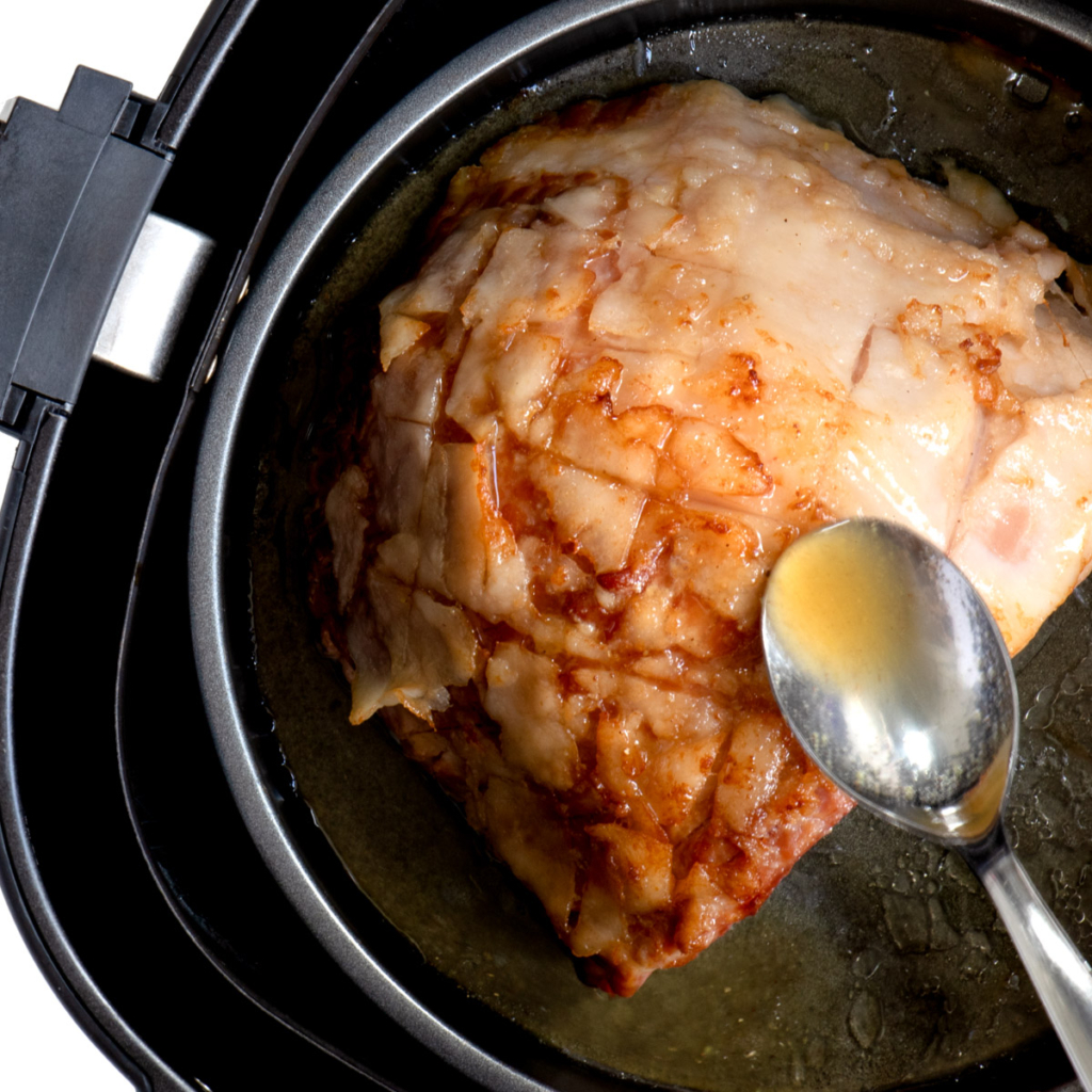 Partially cooked ham in air fryer being glazed.
