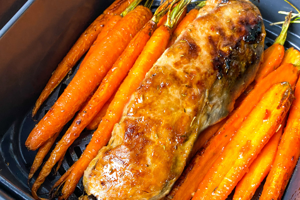 Air fried pork tenderloin in air fryer basket with roasted carrots.