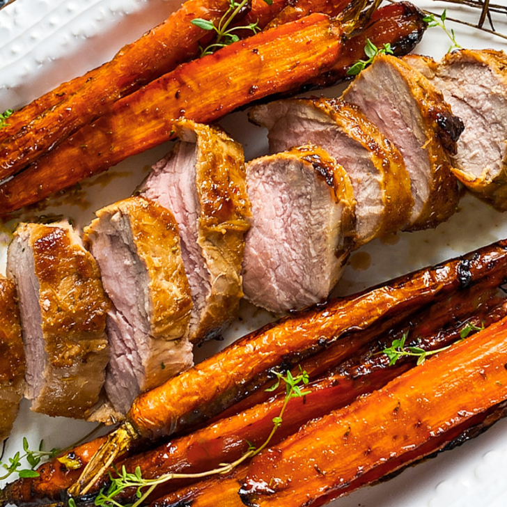Air fryer pork tenderloin on a white plate with roasted carrots.