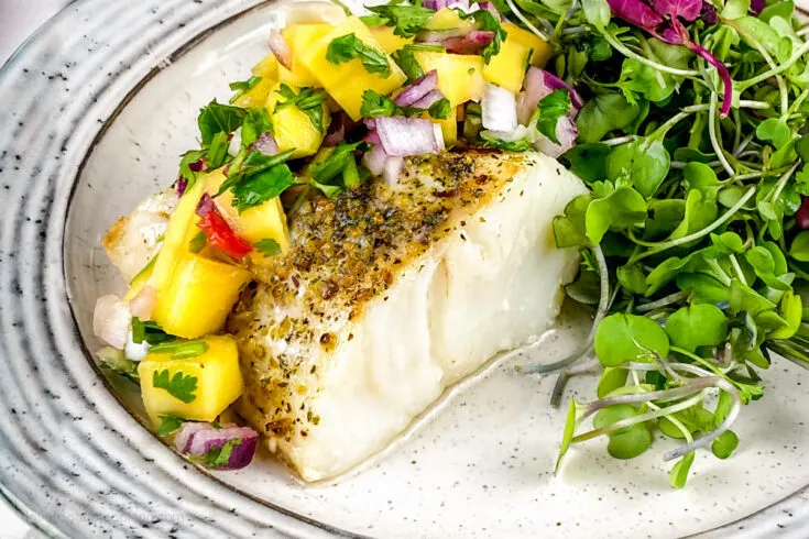 Air fryer white fish on a plate with microgreens and salsa.