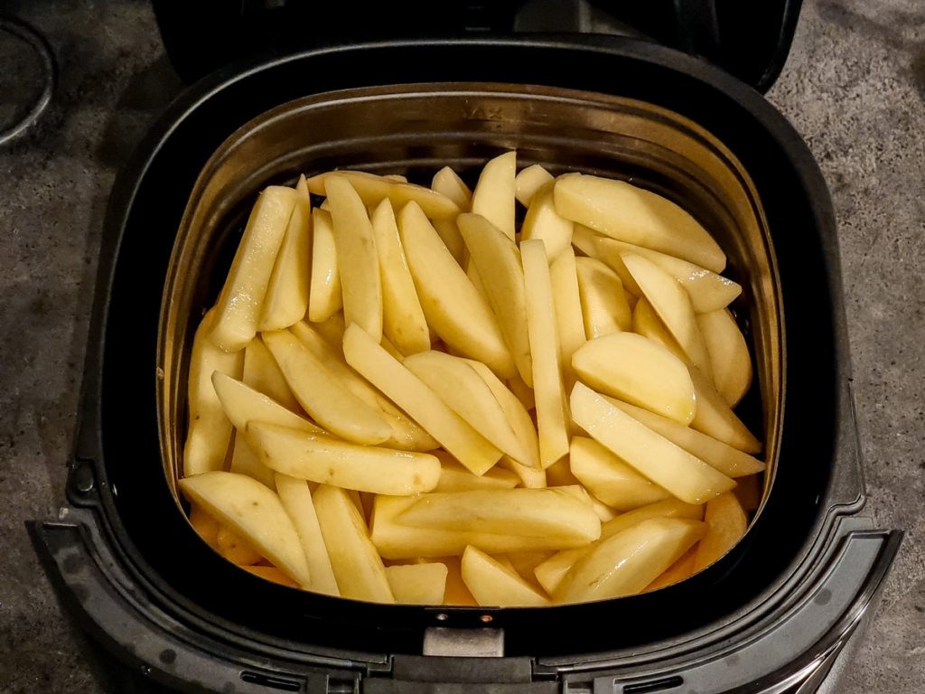 Uncooked french fries in air fryer basket.