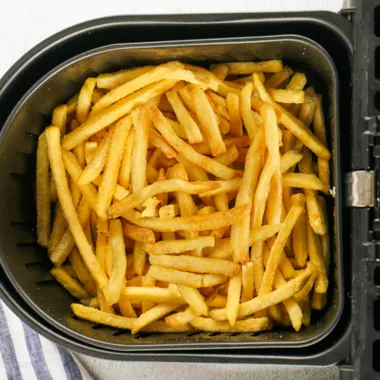 Air fried frozen french fries in air fryer basket.