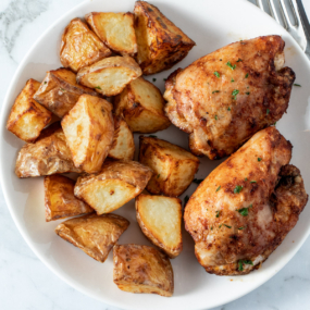 Air fryer chicken thighs and potatoes on a white plate.