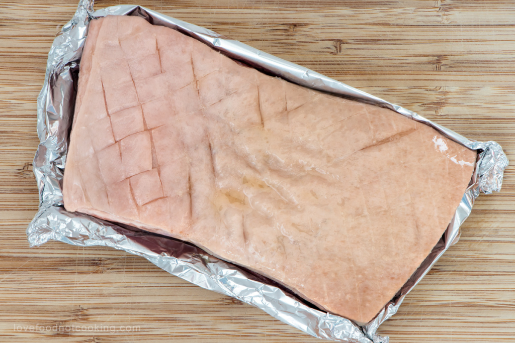Pork belly wrapped in tin foil, the rind is uncovered. 