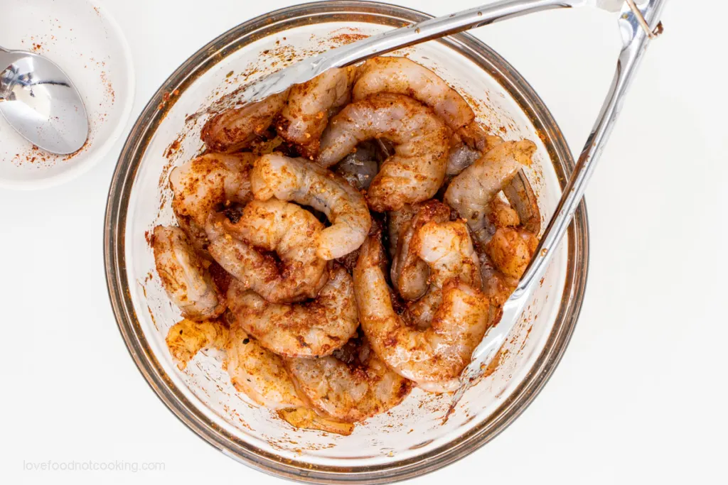 Raw shrimp mixed with seasoning in a glass bowl. 