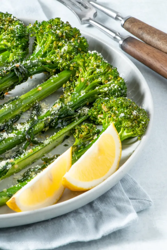 Air fried broccolini on a white plate with lemon wedges. 