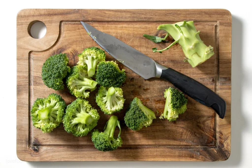 Broccoli being cut into florets on a wooden board.