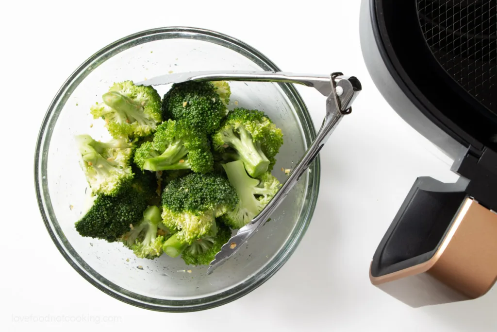 Broccoli florets with oil and seasoning in a glass bowl. 