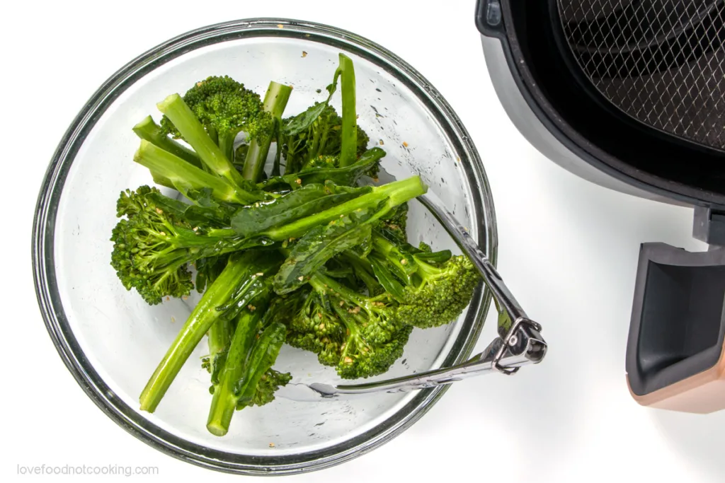 Broccolini in a bowl with oil and seasoning. 