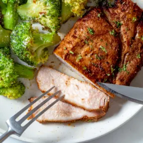 Air fryer pork steaks with broccoli on a white plate.