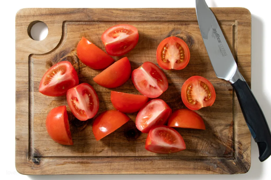 Halved and quarters tomatoes on a wooden board.