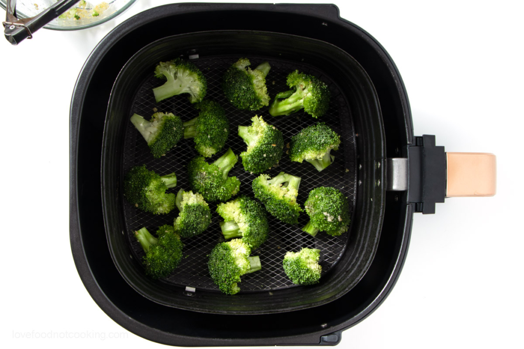 Uncooked broccoli in air fryer basket. 