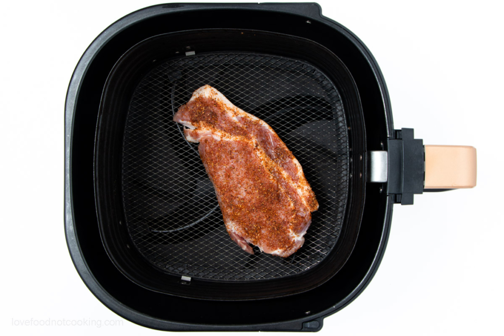 Uncooked pork steak in air fryer basket. 